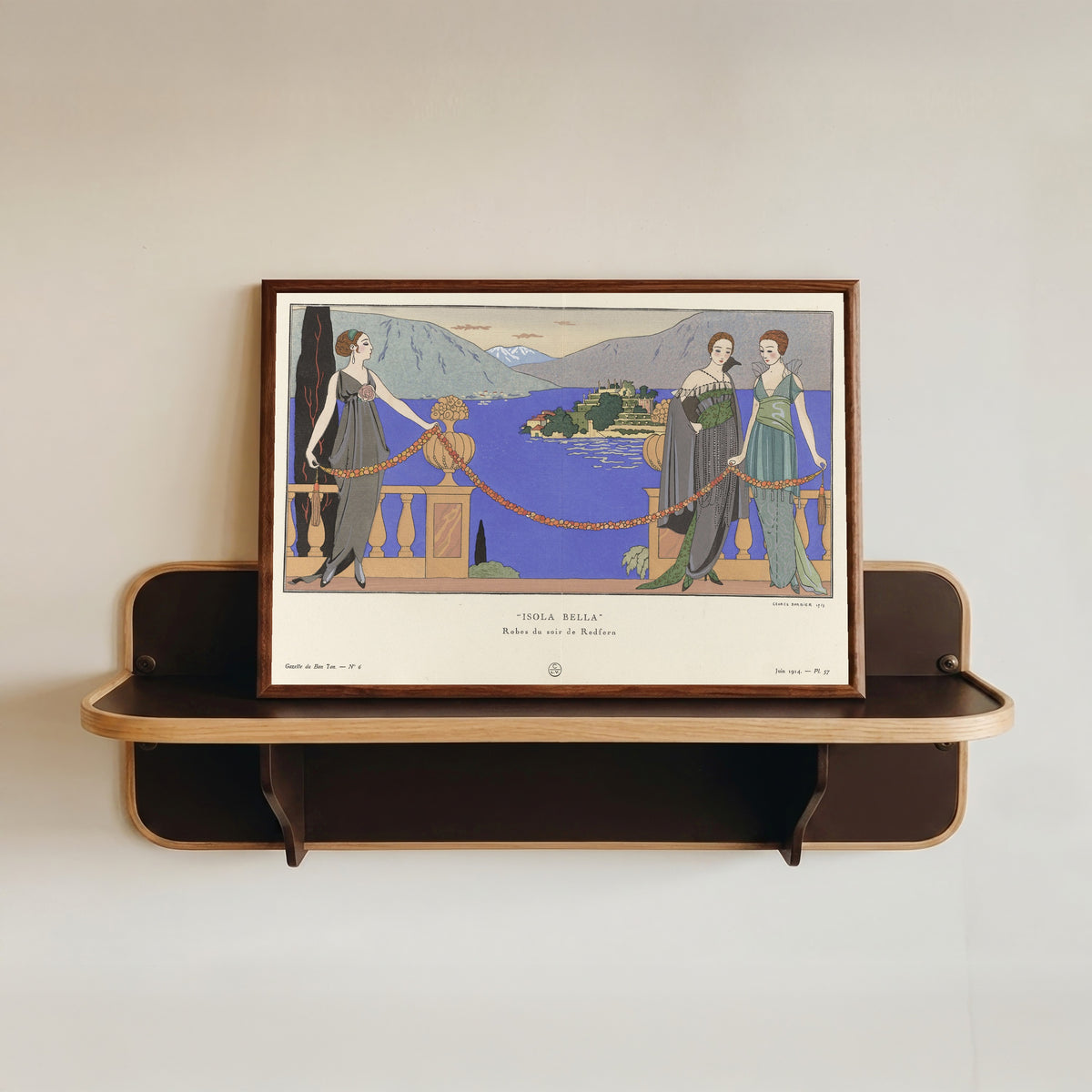 Framed art print of Isola Bella, robes du soir de Redfern by George Barbier, in a dark wood frame resting on a wall shelf