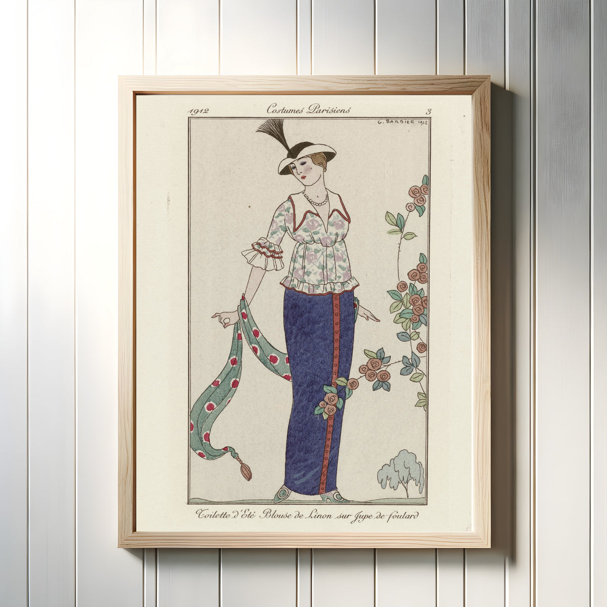 Framed art print of Toilette d'été, blouse de linon sur jupe de foulard [Summer lawn blouse… by George Barbier, in a light wood frame on a white panelled wall