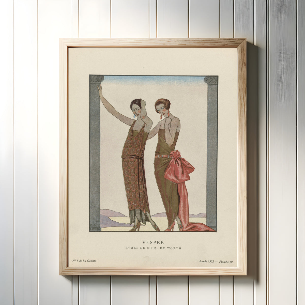 Framed art print of Vesper, robes du soir de Worth by George Barbier, in a light wood frame on a white panelled wall