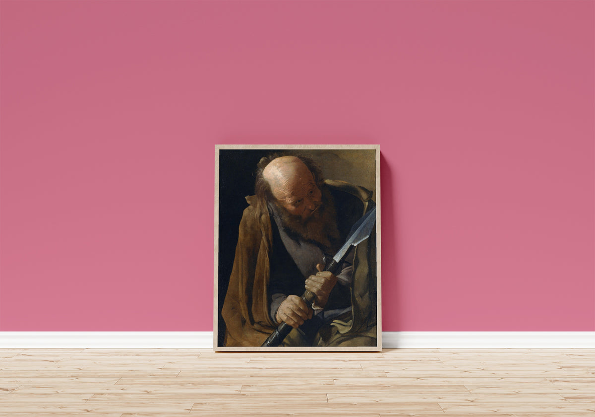 Framed art print of St. Thomas by Georges de La Tour, in a light wood frame leaning on a pink wall above a wooden floor