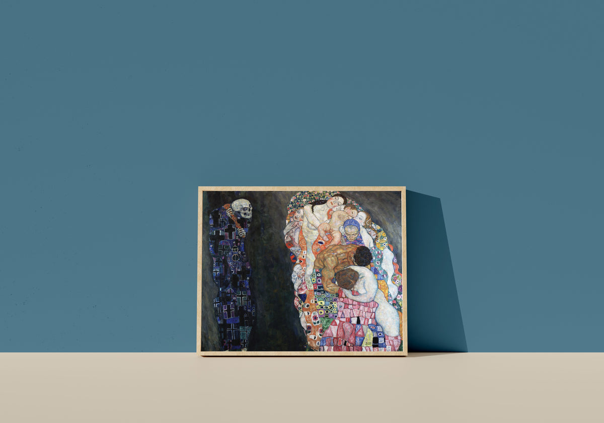 Framed art print of Death and Life by Gustav Klimt, in a light wood frame leaning on a blue wall