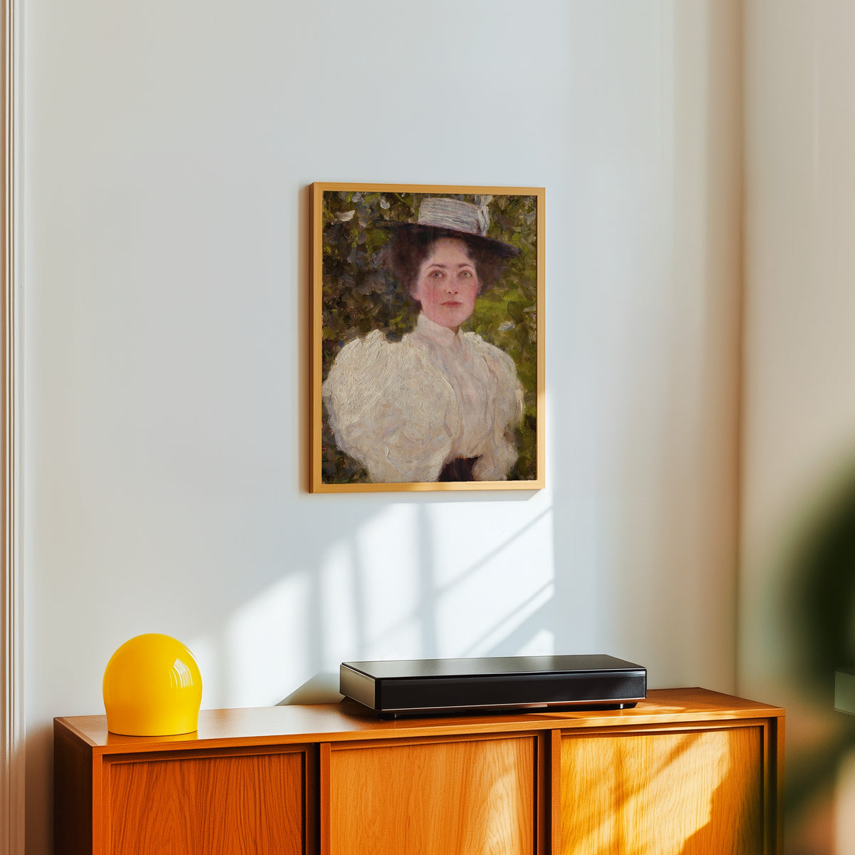 Framed art print of Girl in the Foliage (Mädchen im Grünen) by Gustav Klimt, in a light wood frame on a white wall above an orange sideboard