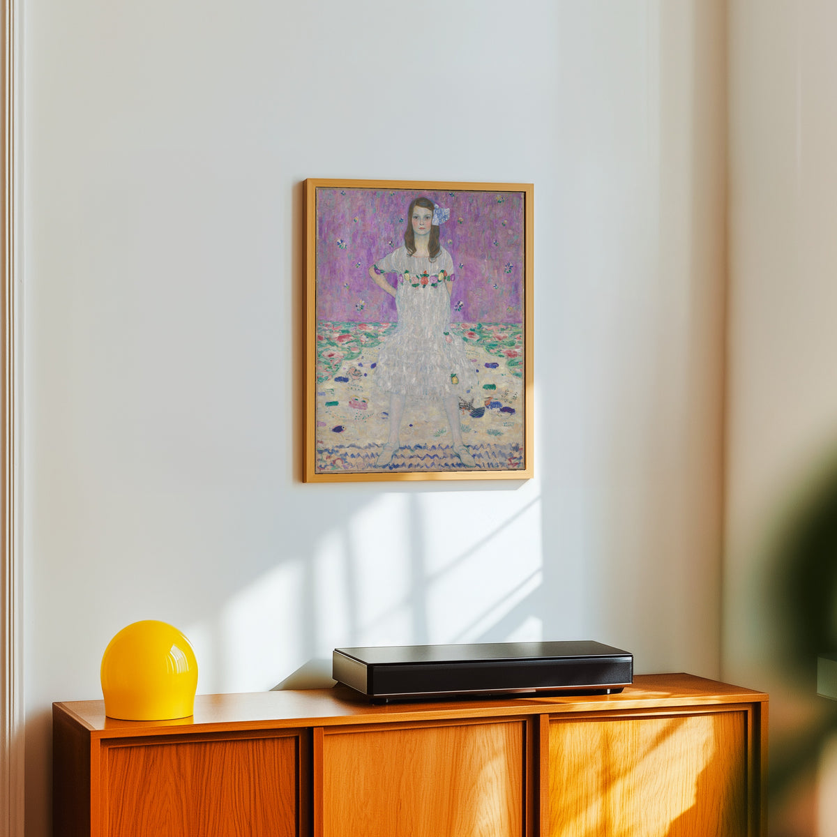 Framed art print of Portrait of Mäda Primavesi by Gustav Klimt, in a light wood frame on a white wall above an orange sideboard
