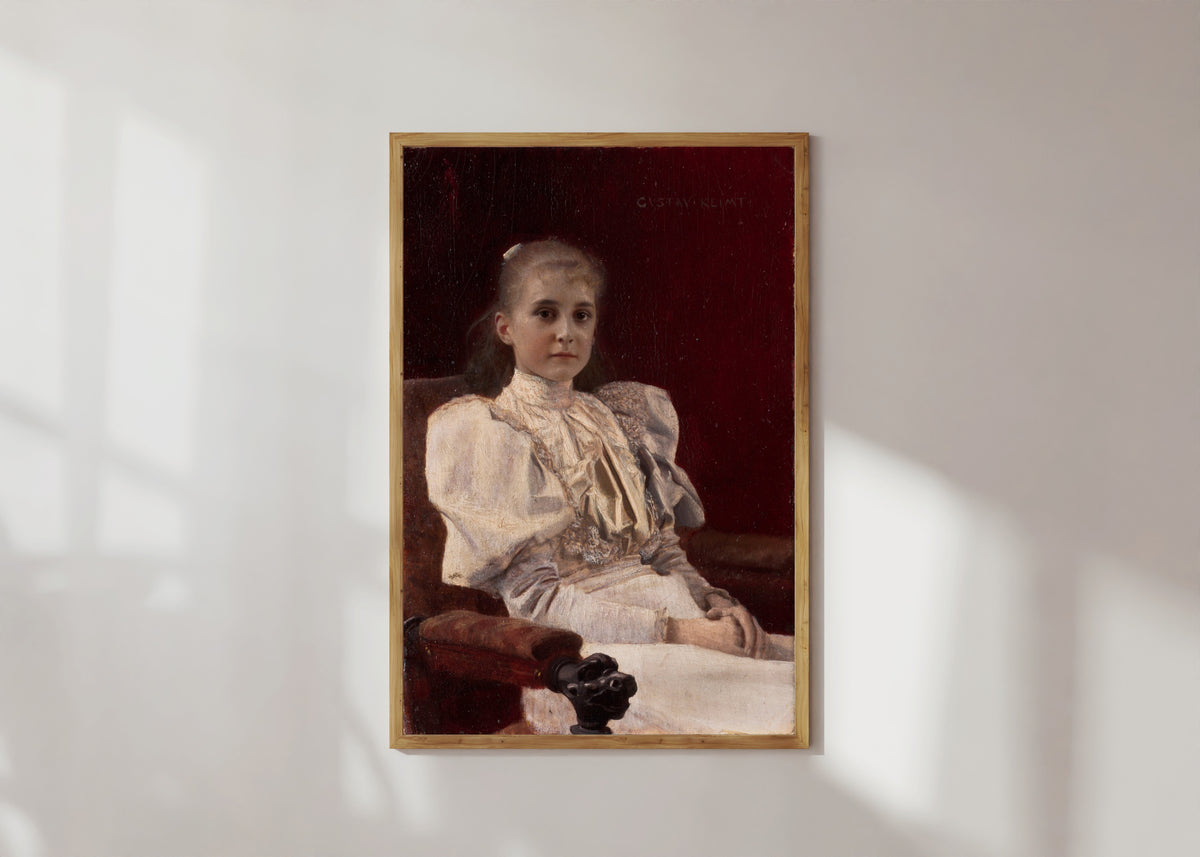 Framed art print of Seated Young Girl by Gustav Klimt, in a light wood frame on a sunlit white wall