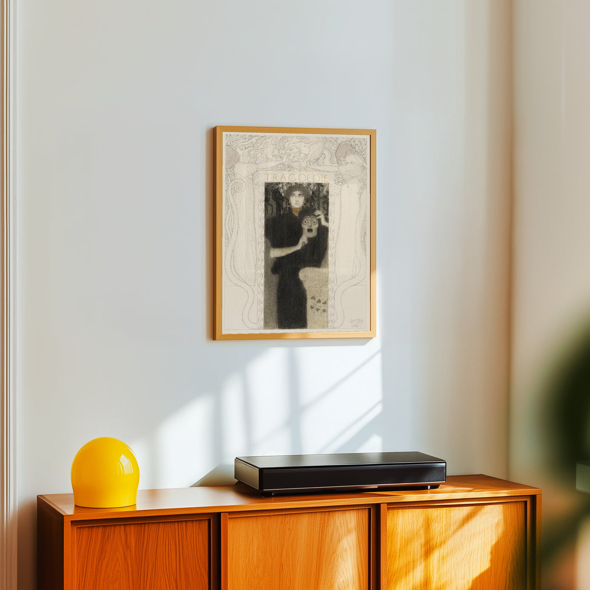 Framed art print of Tragedy (Tragödie) by Gustav Klimt, in a light wood frame on a white wall above an orange sideboard