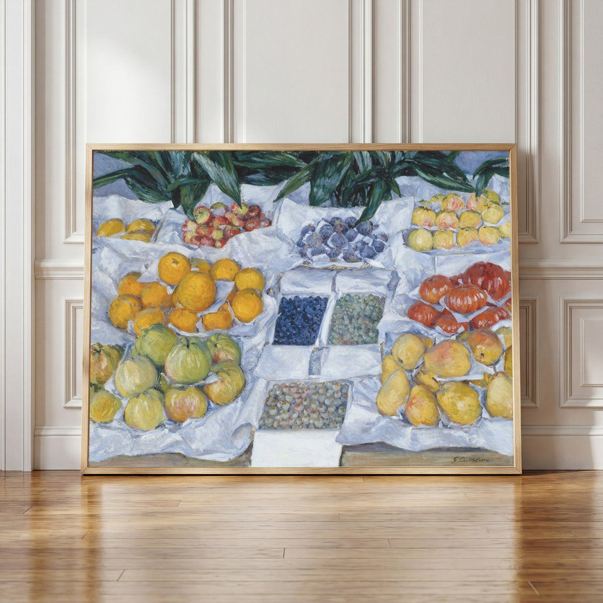Framed art print of Fruit Displayed on a Stand by Gustave Caillebotte, in a light wood frame leaning against a panelled white wall