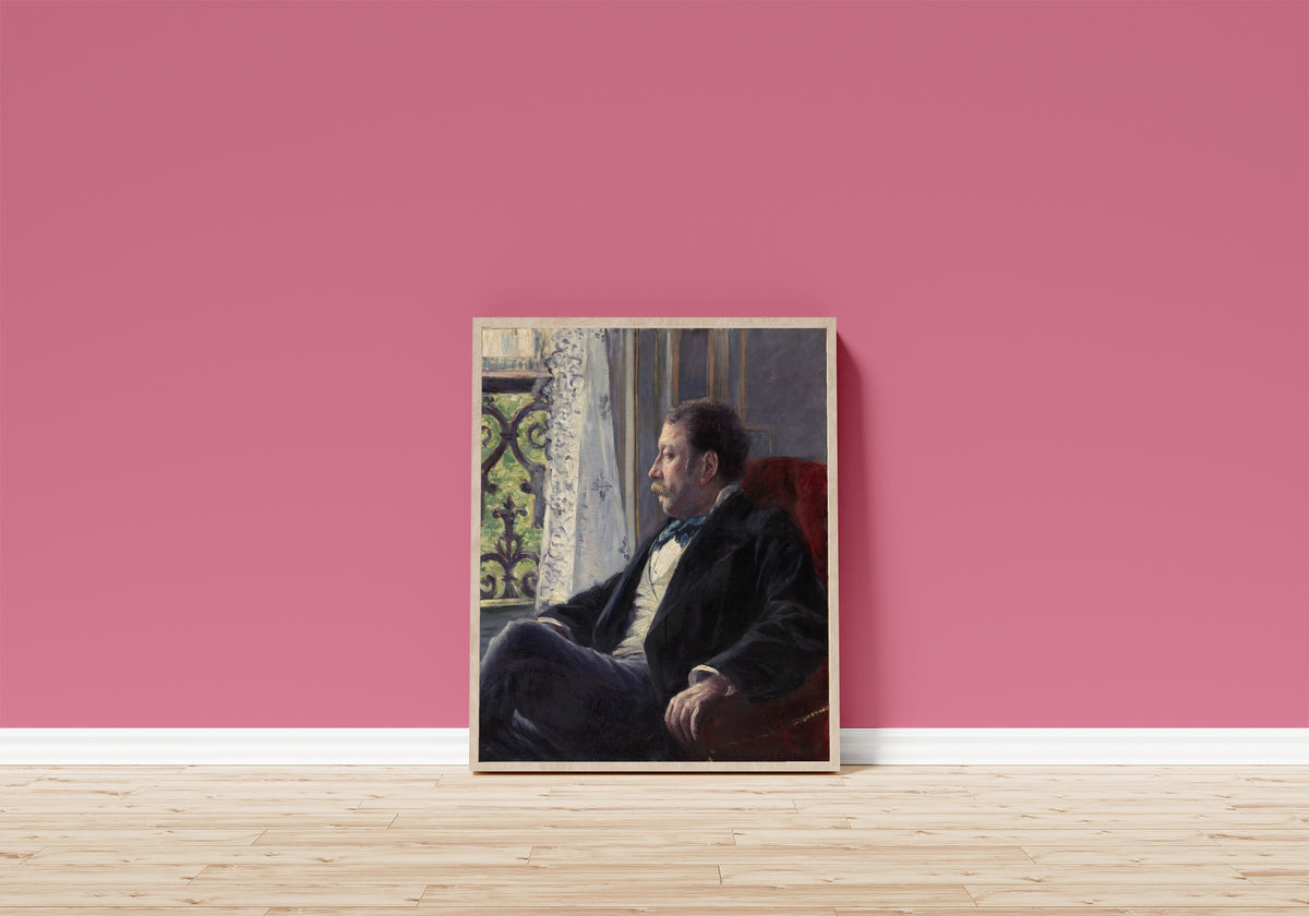 Framed art print of Portrait of a Man by Gustave Caillebotte, in a light wood frame leaning on a pink wall above a wooden floor