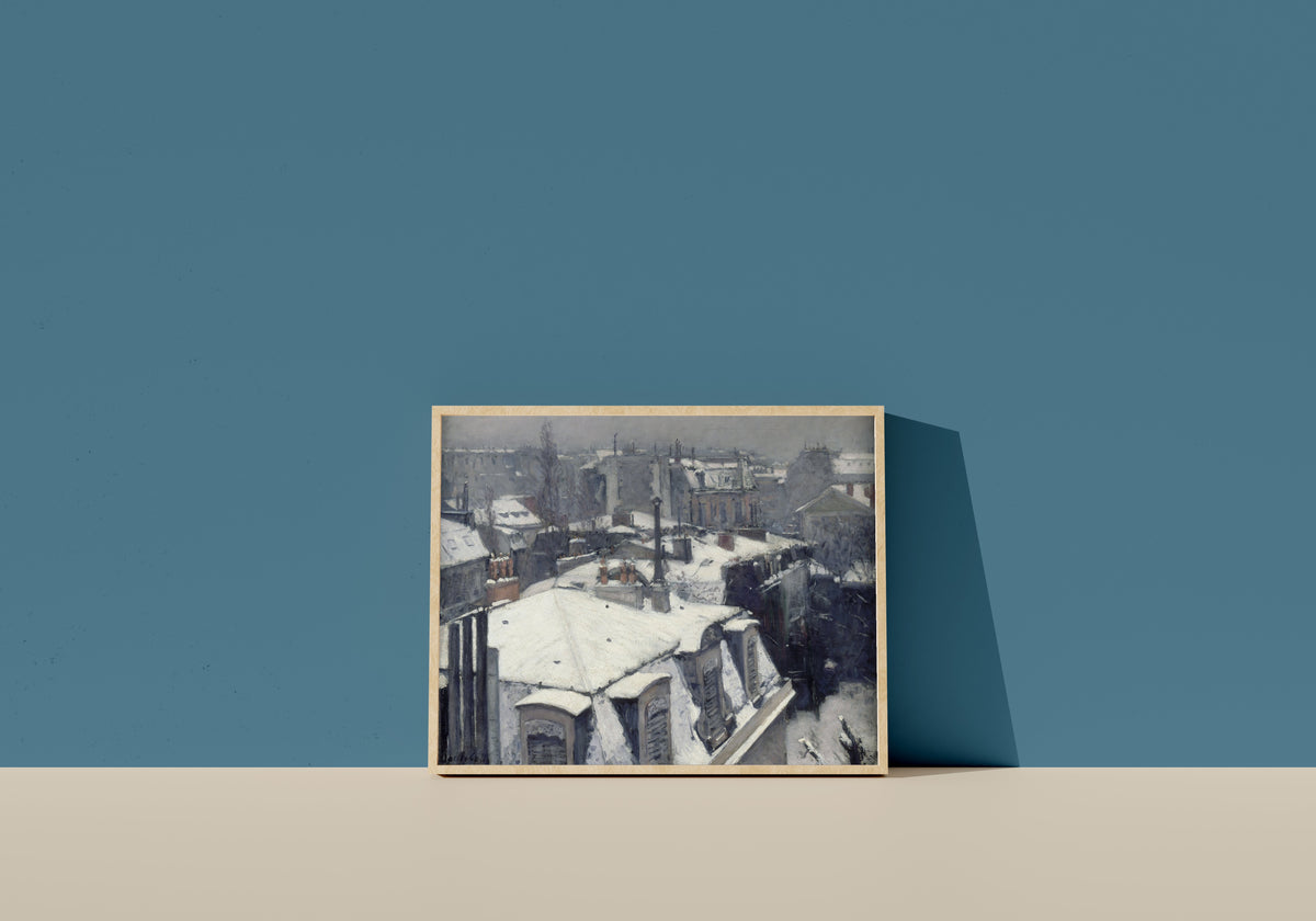 Framed art print of Rooftops in the Snow (Snow Effect) by Gustave Caillebotte, in a light wood frame leaning on a blue wall