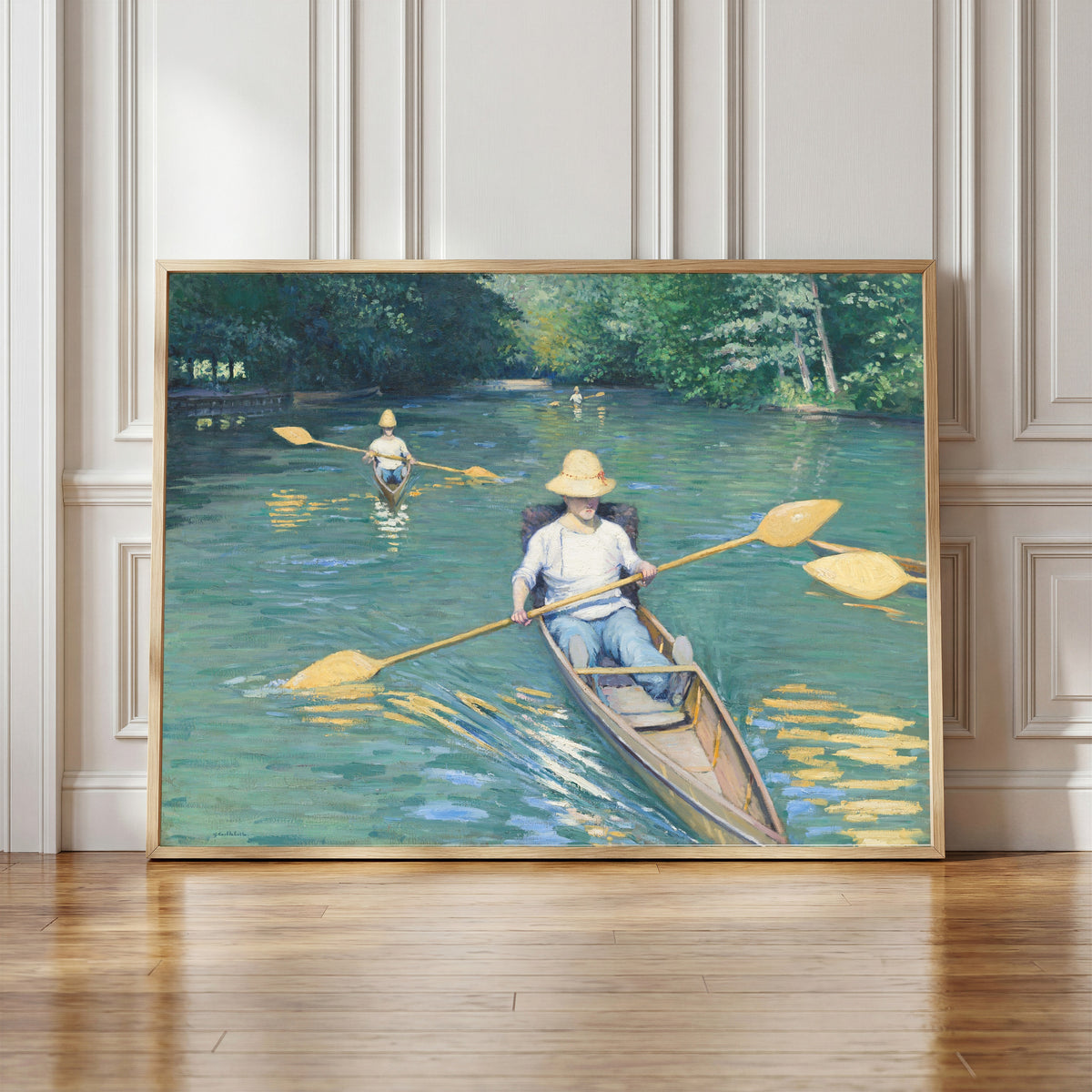 Framed art print of Skiffs by Gustave Caillebotte, in a light wood frame leaning against a panelled white wall