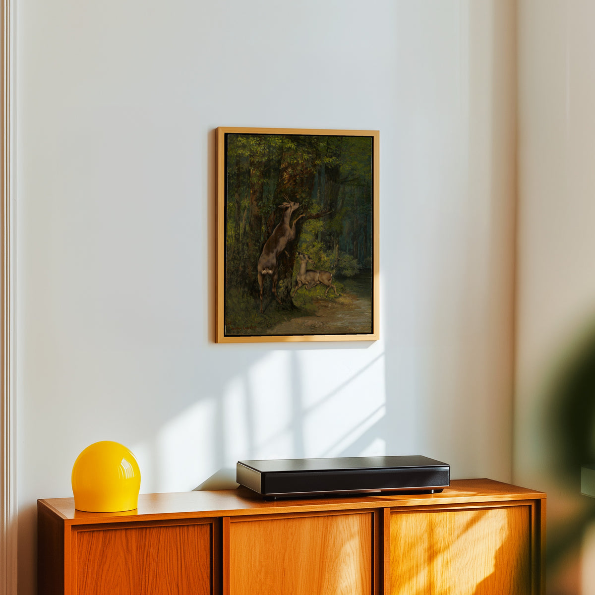 Framed art print of Deer in the Forest by Gustave Courbet, in a light wood frame on a white wall above an orange sideboard