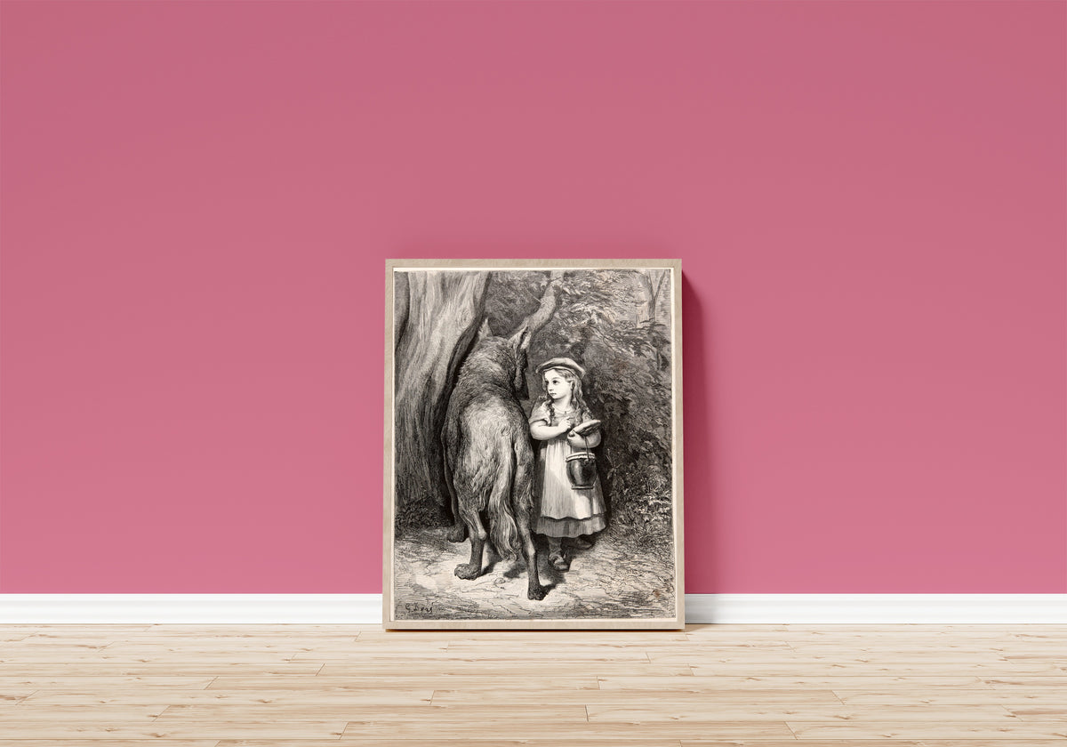 Framed art print of Little Red Riding Hood: Meeting the Wolf by Gustave Doré, in a light wood frame leaning on a pink wall above a wooden floor