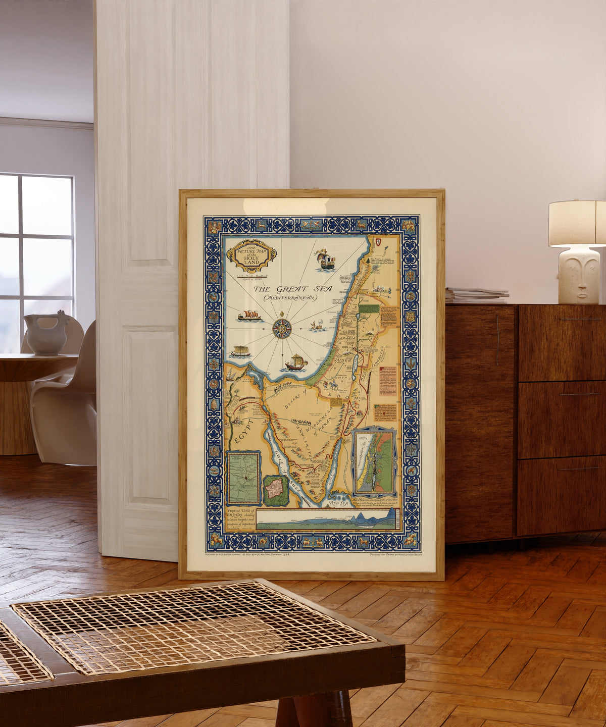 Framed art print of The Picture Map of the Holy Land by Harold Haven Brown, in a light wood frame leaning in a warm room with a parquet floor