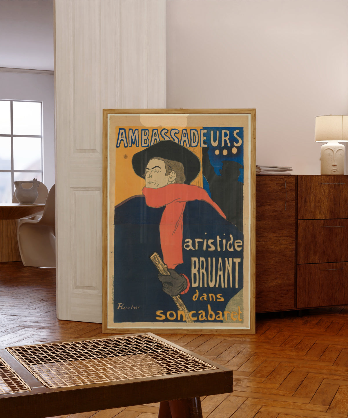 Framed art print of Ambassadeurs: Aristide Bruant by Henri de Toulouse-Lautrec, in a light wood frame leaning in a warm room with a parquet floor