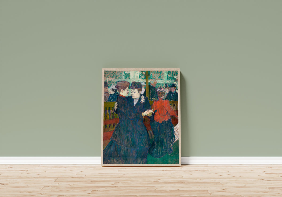 Framed art print of At the Moulin Rouge: Two Women… by Henri de Toulouse-Lautrec, in a light wood frame leaning on a sage green wall above a wooden floor