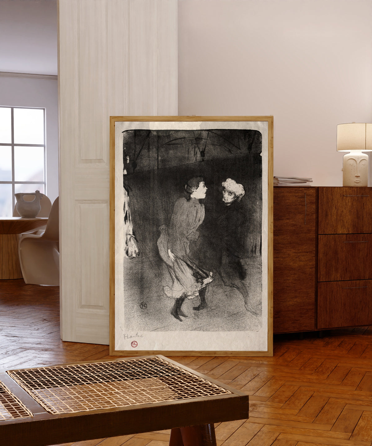 Framed art print of Emilienne d'Alençon and Mariquita of the… by Henri de Toulouse-Lautrec, in a light wood frame leaning in a warm room with a parquet floor