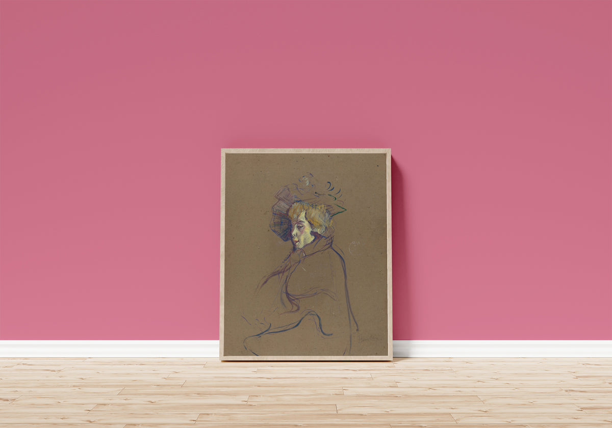 Framed art print of Jane Avril (Profile in a Plumed Hat) by Henri de Toulouse-Lautrec, in a light wood frame leaning on a pink wall above a wooden floor