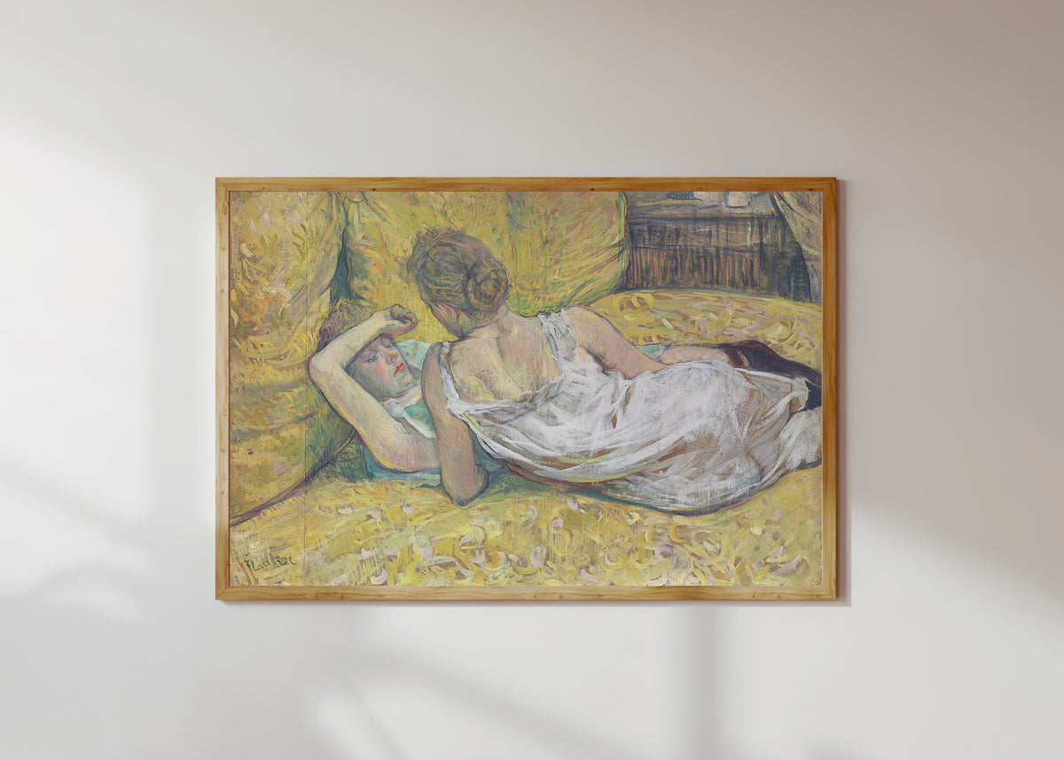 Framed art print of L'Abandon (Les Deux Amies) by Henri de Toulouse-Lautrec, in a light wood frame on a sunlit white wall