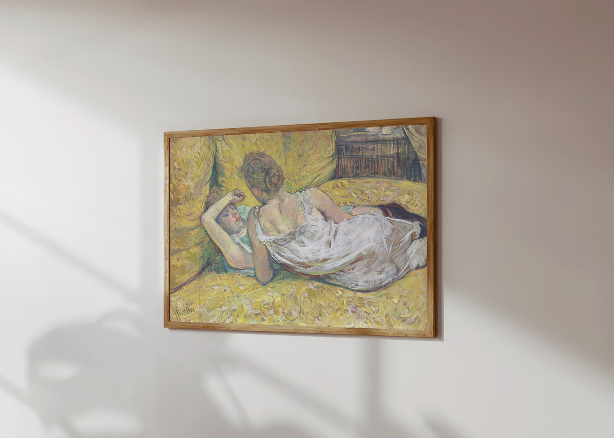 Framed art print of L'Abandon (Les Deux Amies) by Henri de Toulouse-Lautrec, in a light wood frame on a sunlit white wall, seen at a slight angle