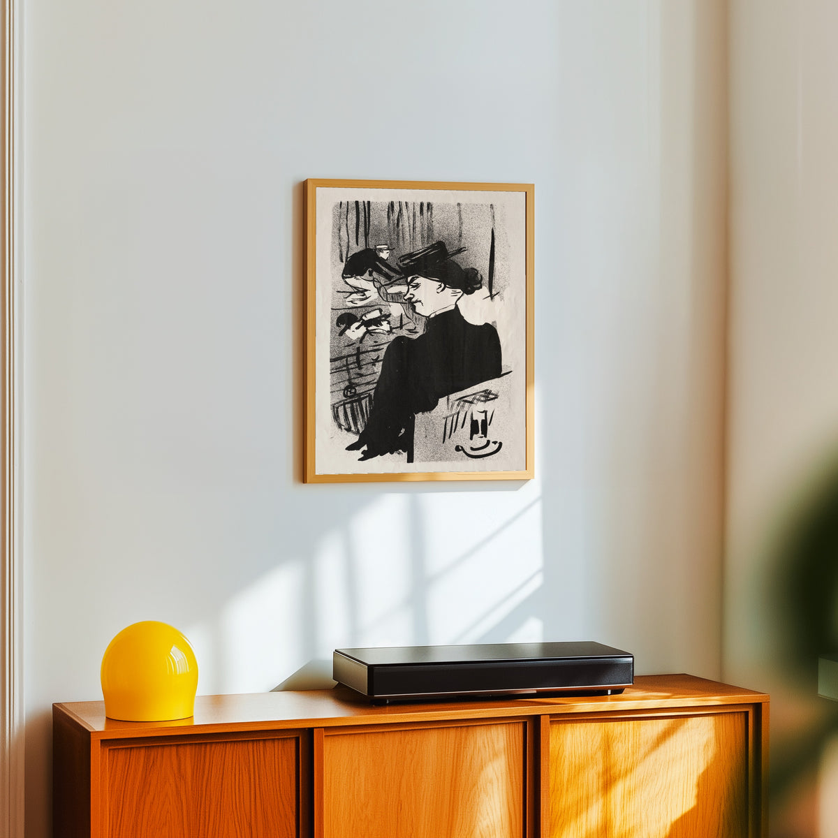 Framed art print of Le Café-Concert: Une Spectatrice by Henri de Toulouse-Lautrec, in a light wood frame on a white wall above an orange sideboard