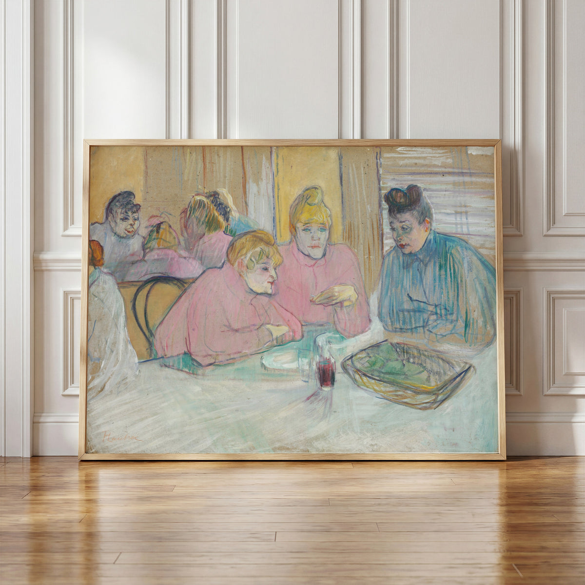 Framed art print of These Ladies in the Dining Room by Henri de Toulouse-Lautrec, in a light wood frame leaning against a panelled white wall