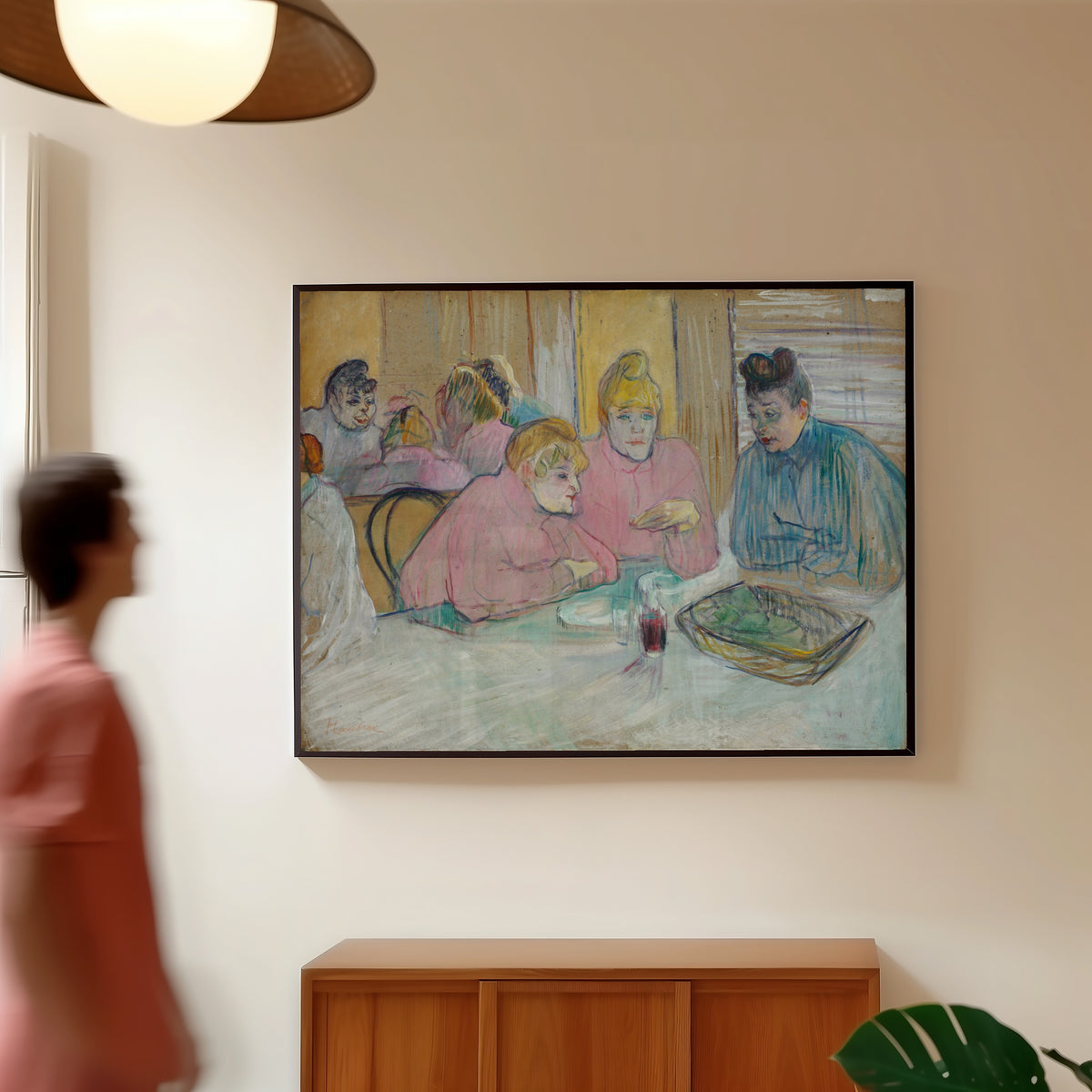 Framed art print of These Ladies in the Dining Room by Henri de Toulouse-Lautrec, in a slim black frame on a warm wall in a sunlit room