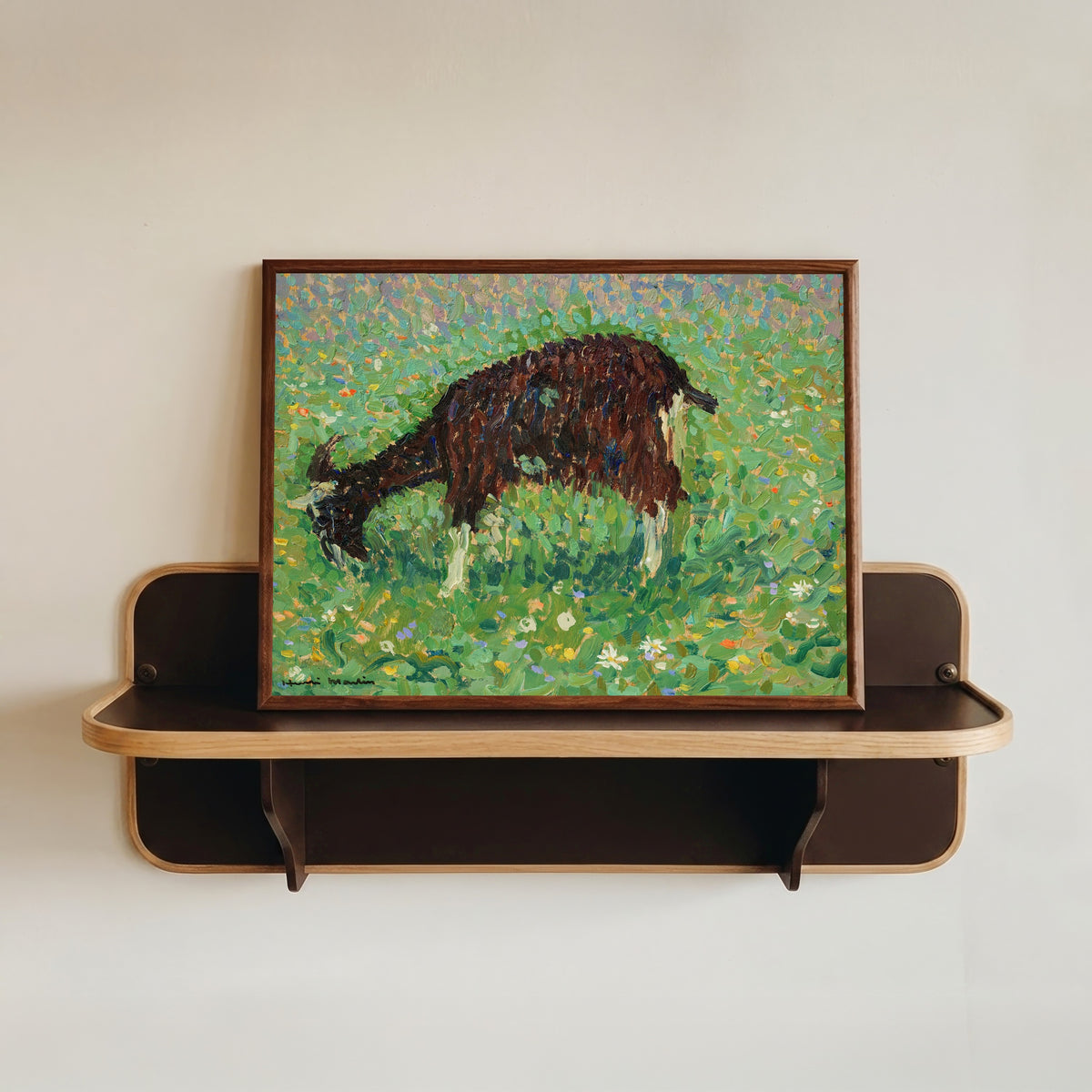 Framed art print of Chèvre dans un champ de fleurs by Henri Martin, in a dark wood frame resting on a wall shelf