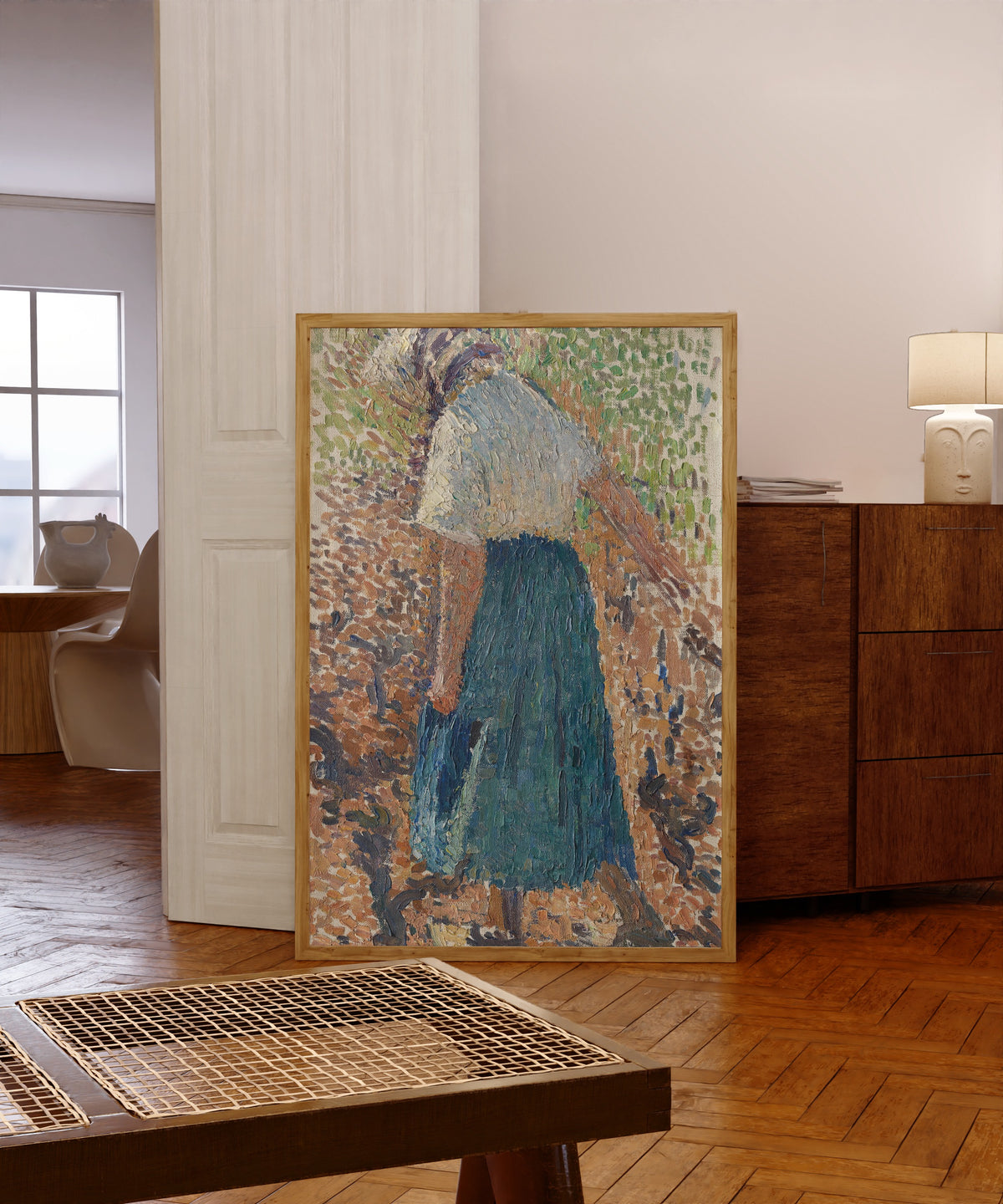 Framed art print of Jeune femme dans les vignes by Henri Martin, in a light wood frame leaning in a warm room with a parquet floor