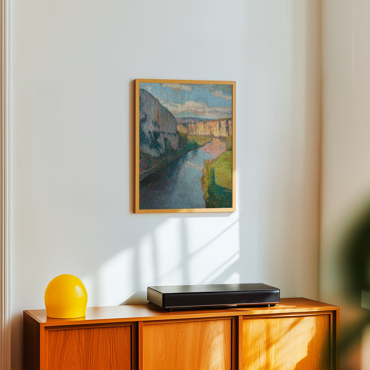 Framed art print of La Vallée du Lot, près de Saint-Cirq-Lapopie (Clouds over… by Henri Martin, in a light wood frame on a white wall above an orange sideboard