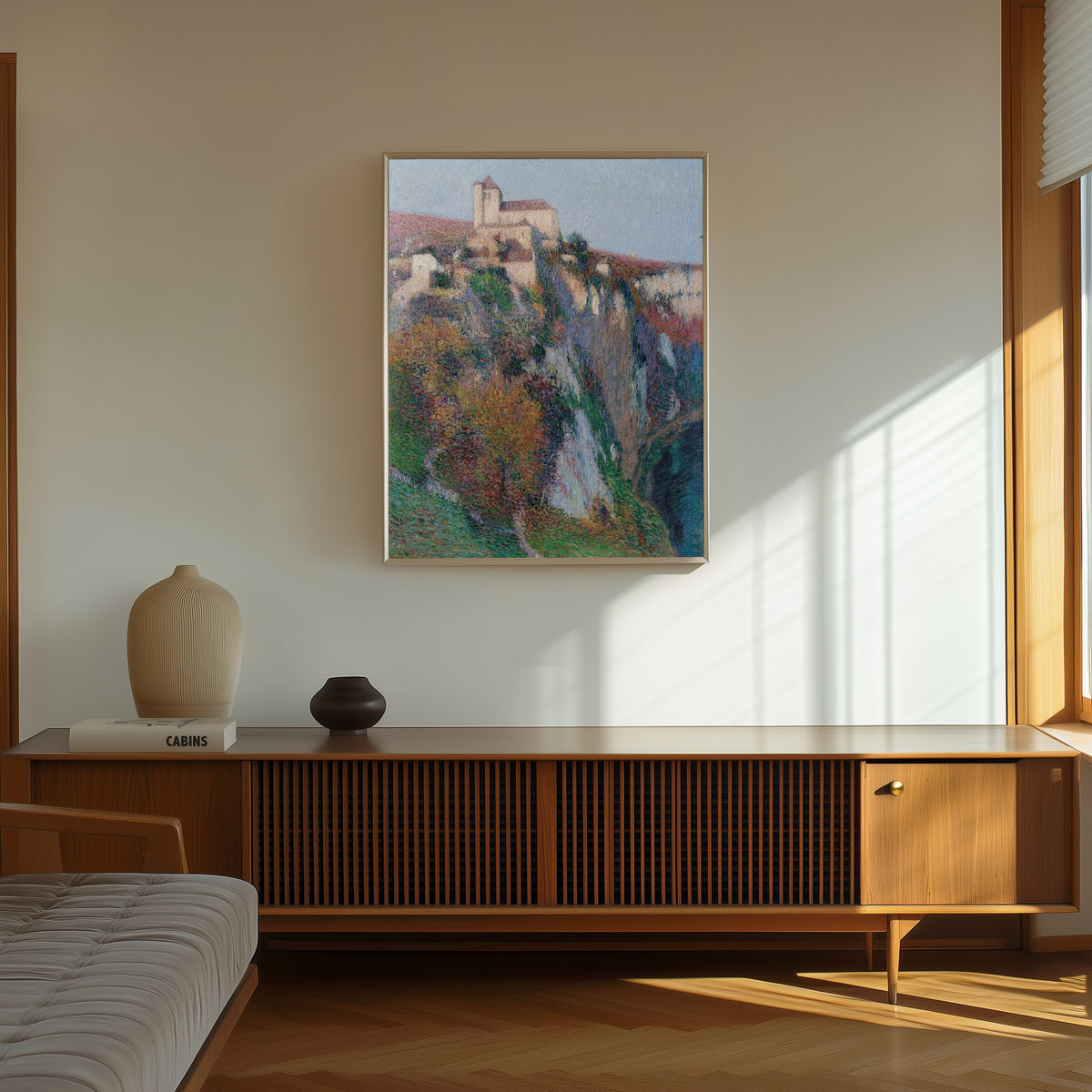 Framed art print of L'église Saint-Cirq Lapopie perchée sur la falaise de la… by Henri Martin, in a thin light frame on a sunlit wall above a wooden sideboard