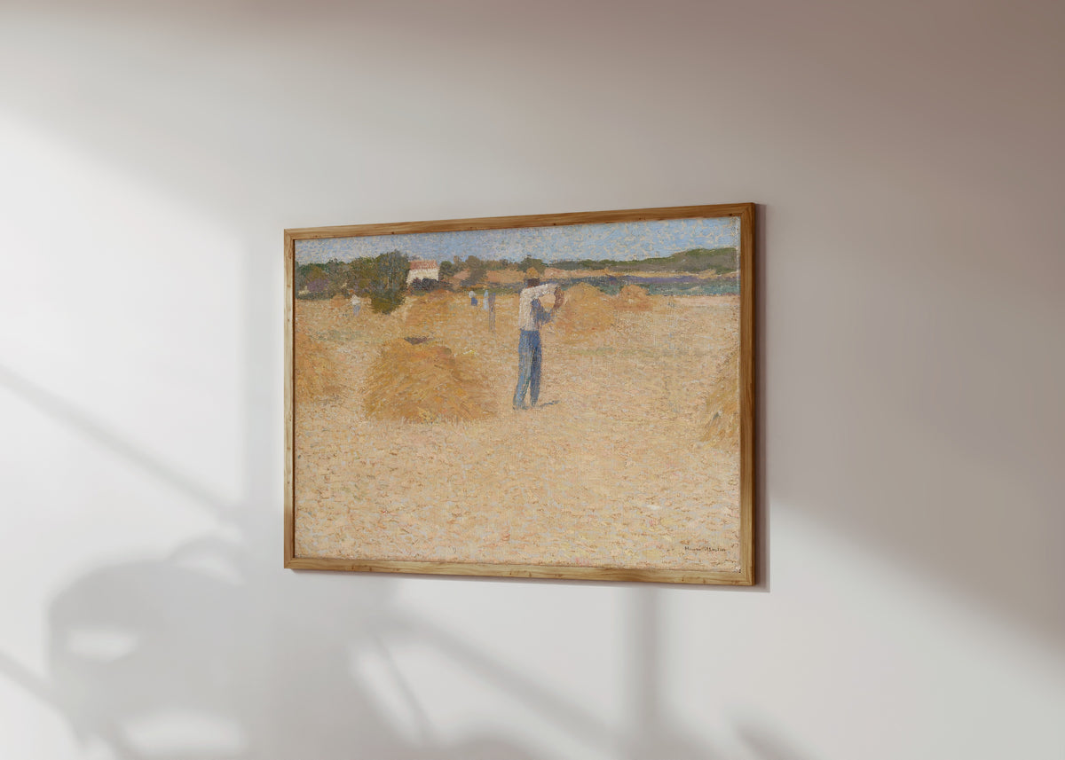 Framed art print of Les Moissons de blé by Henri Martin, in a light wood frame on a sunlit white wall, seen at a slight angle