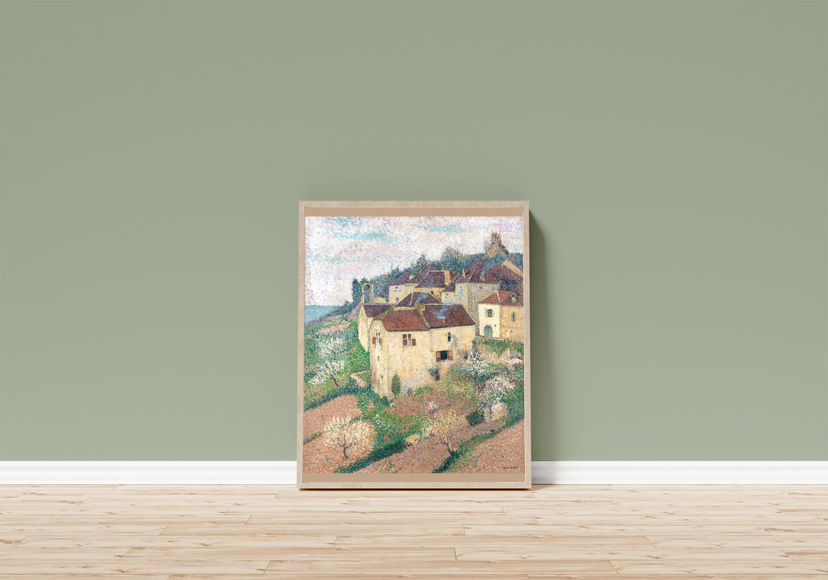 Framed art print of Maisons à Saint-Cirq-Lapopie by Henri Martin, in a light wood frame leaning on a sage green wall above a wooden floor