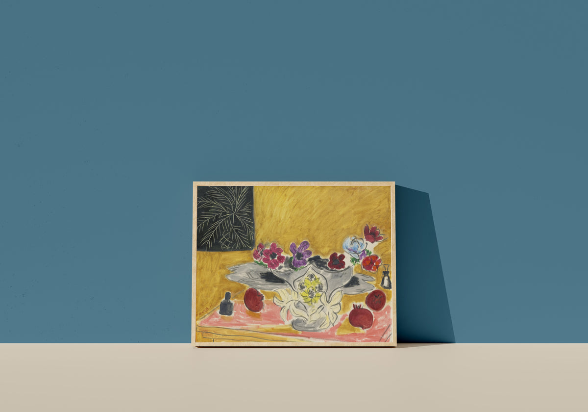 Framed art print of Anemones and Pomegranates by Henri Matisse, in a light wood frame leaning on a blue wall