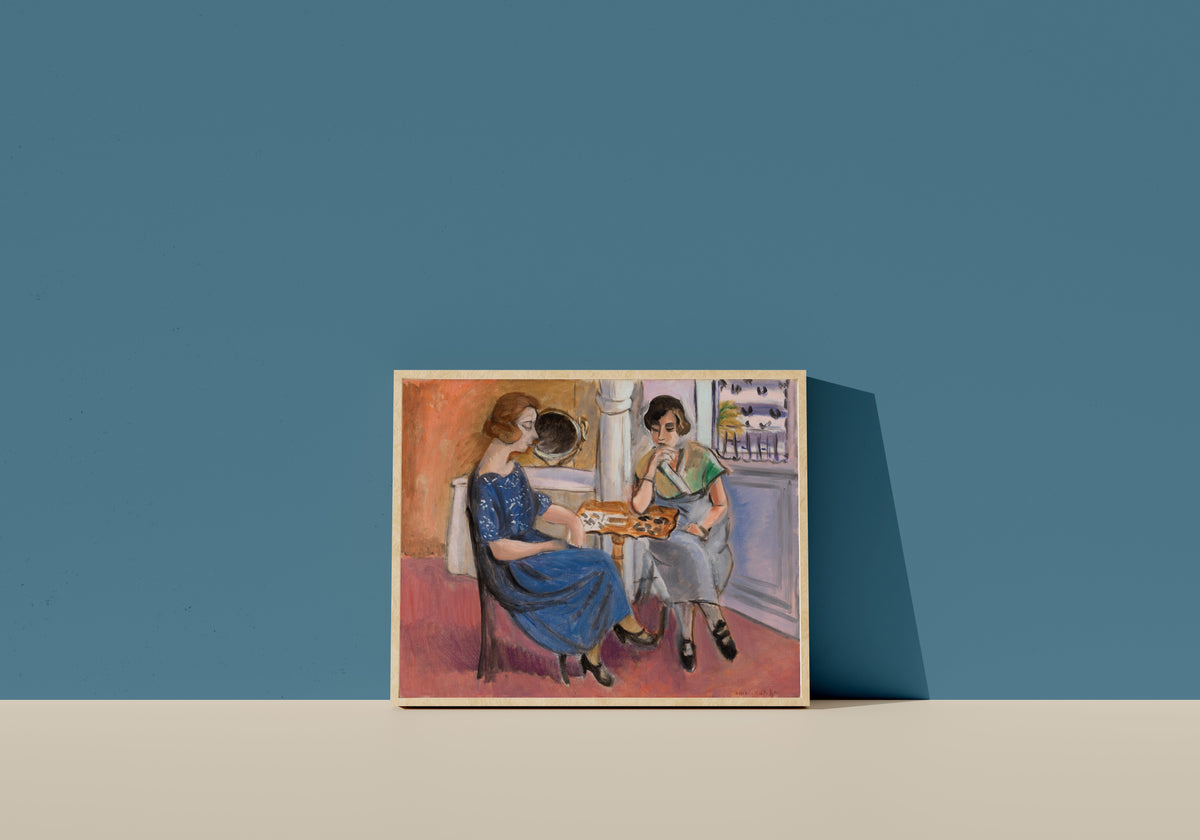 Framed art print of Domino Players by Henri Matisse, in a light wood frame leaning on a blue wall