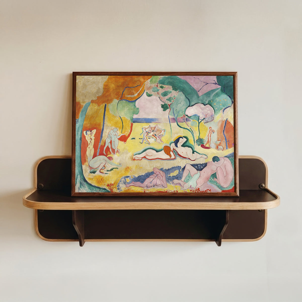 Framed art print of Le Bonheur de vivre (The Joy of Life) by Henri Matisse, in a dark wood frame resting on a wall shelf