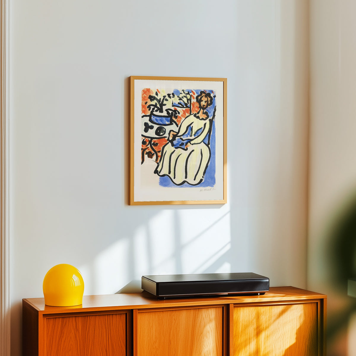 Framed art print of Marie-José in a Yellow Dress by Henri Matisse, in a light wood frame on a white wall above an orange sideboard