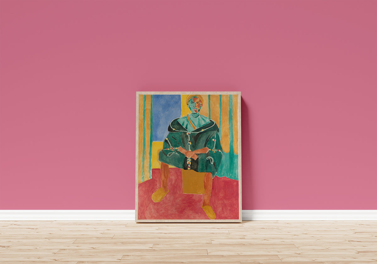 Framed art print of Seated Riffian by Henri Matisse, in a light wood frame leaning on a pink wall above a wooden floor