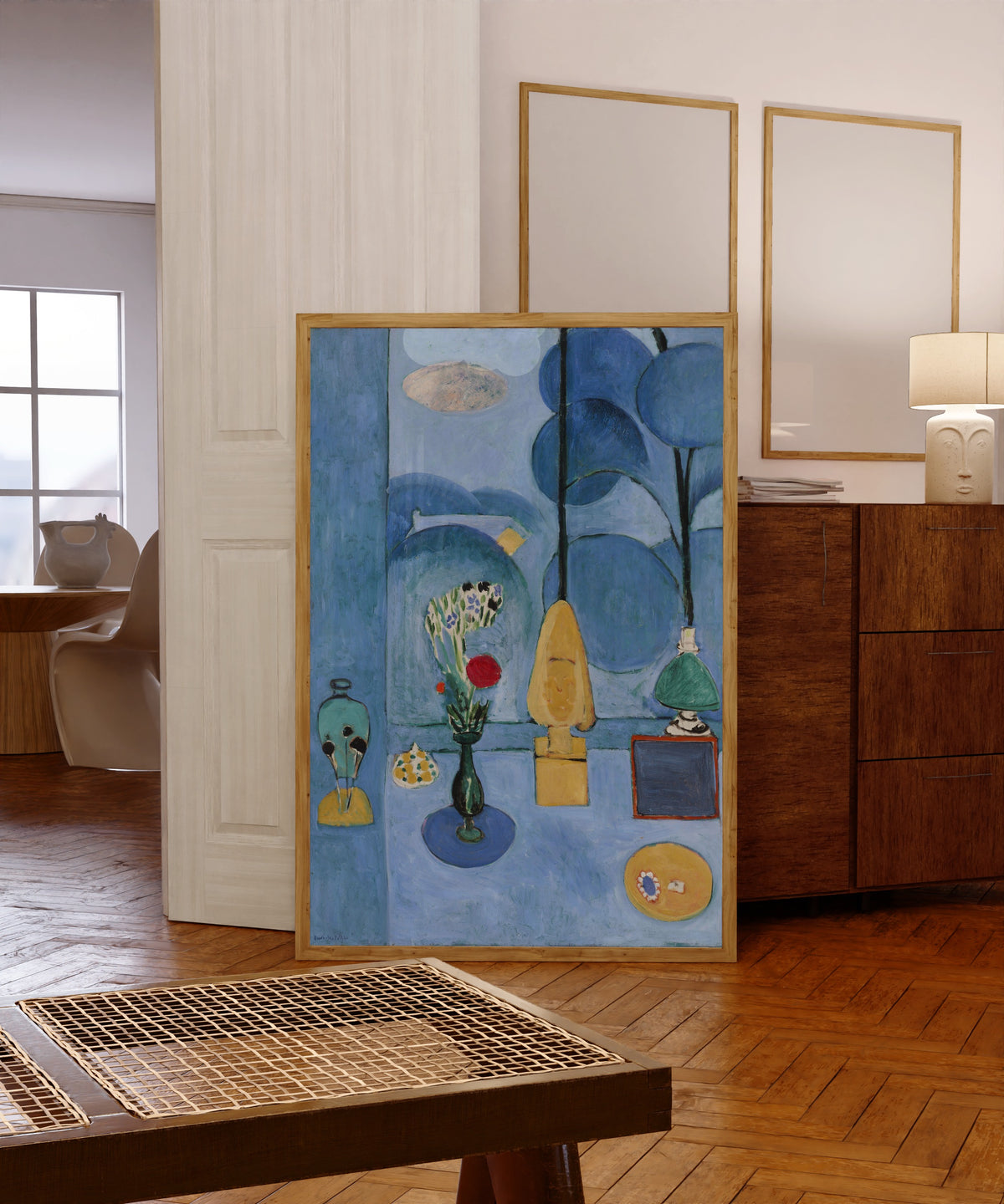 Framed art print of The Blue Window (La Glace sans tain) by Henri Matisse, in a light wood frame leaning in a warm room with a parquet floor