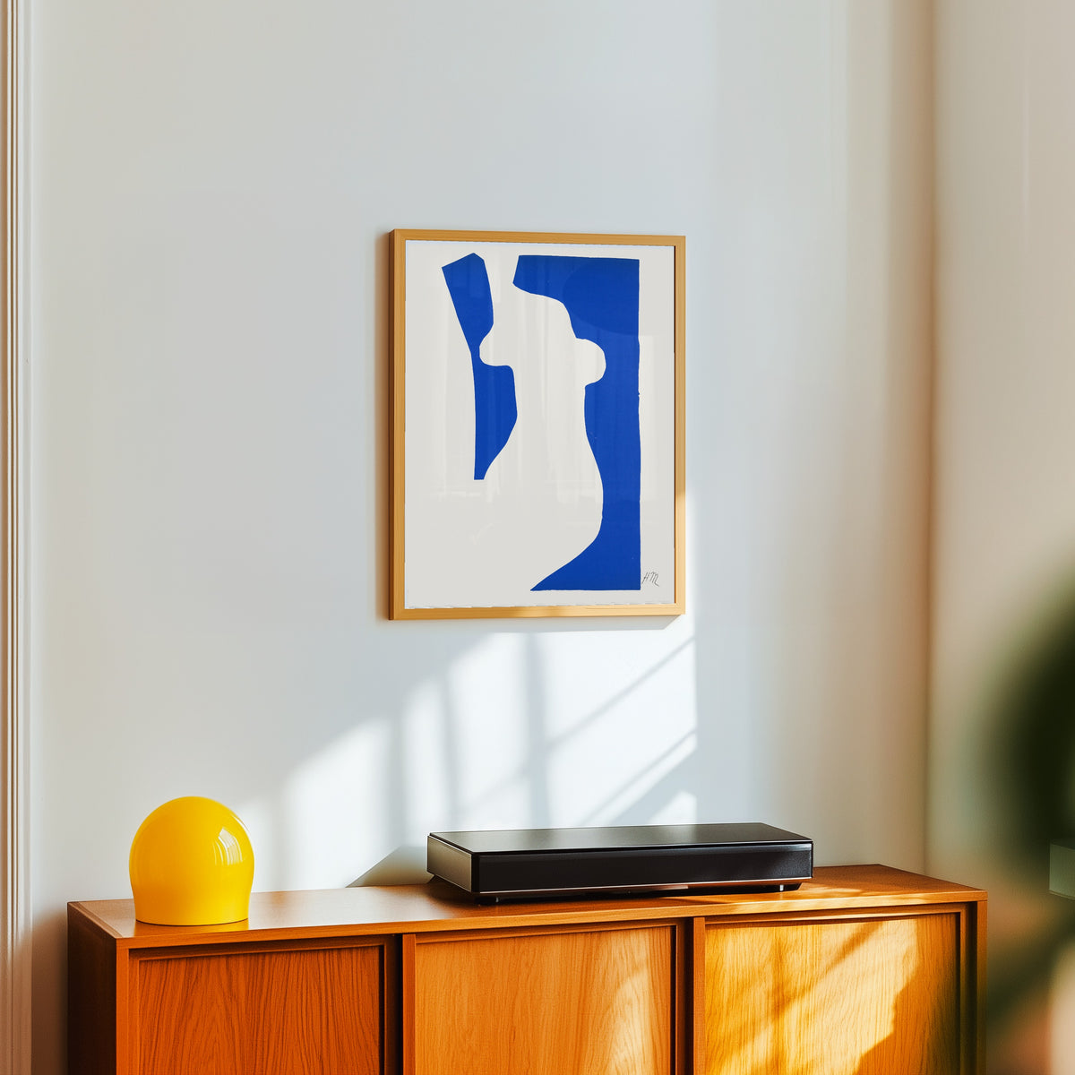 Framed art print of Venus by Henri Matisse, in a light wood frame on a white wall above an orange sideboard