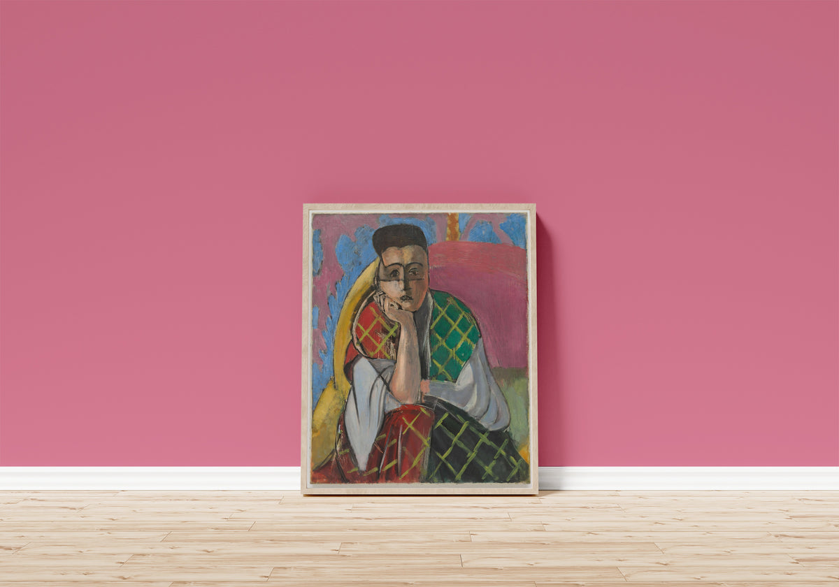 Framed art print of Woman with a Veil by Henri Matisse, in a light wood frame leaning on a pink wall above a wooden floor