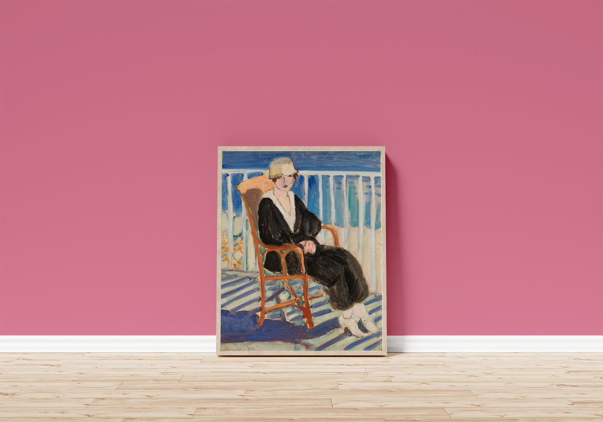 Framed art print of Young Girl on a Balcony over the Ocean by Henri Matisse, in a light wood frame leaning on a pink wall above a wooden floor