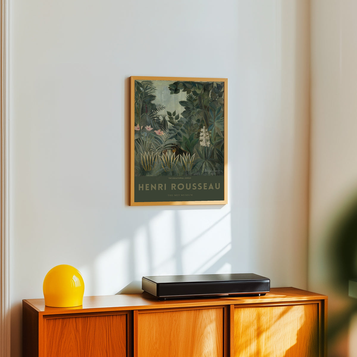 Framed art print of The Equatorial Jungle by Henri Rousseau, in a light wood frame on a white wall above an orange sideboard