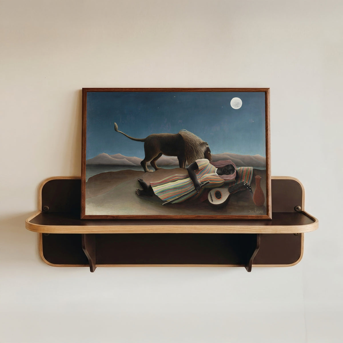 Framed art print of The Sleeping Gypsy by Henri Rousseau, in a dark wood frame resting on a wall shelf