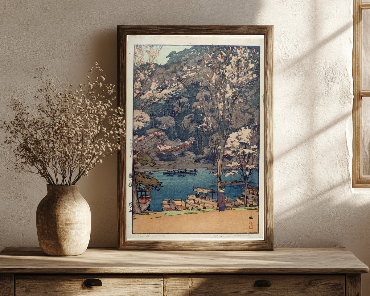 Framed art print of Arashiyama Lake by Hiroshi Yoshida, in a dark wood frame leaning on a rustic console beside dried flowers