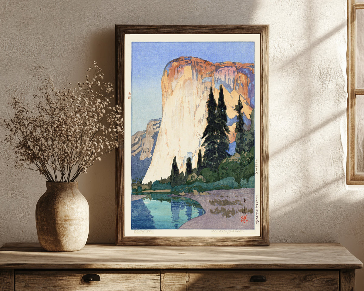 Framed art print of El Capitan by Hiroshi Yoshida, in a dark wood frame leaning on a rustic console beside dried flowers