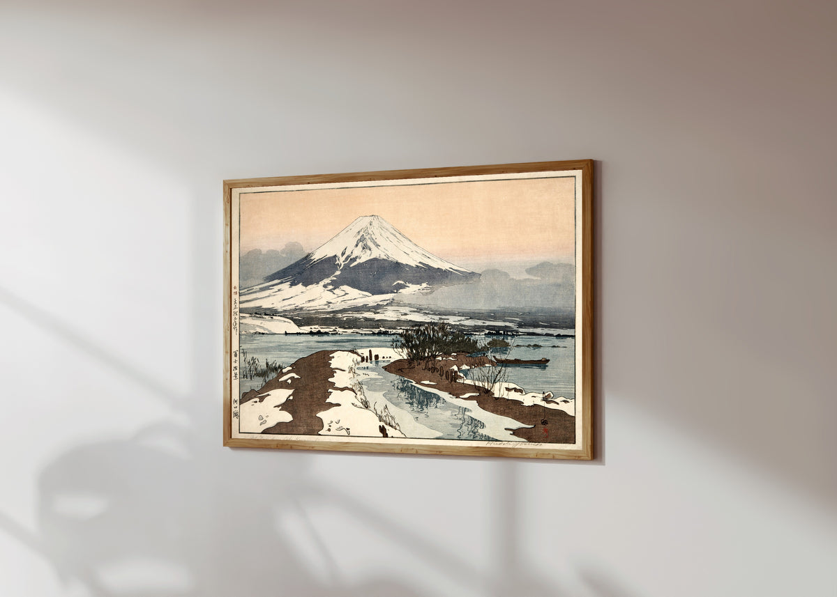 Framed art print of Fuji from Lake Kawaguchi by Hiroshi Yoshida, in a light wood frame on a sunlit white wall, seen at a slight angle