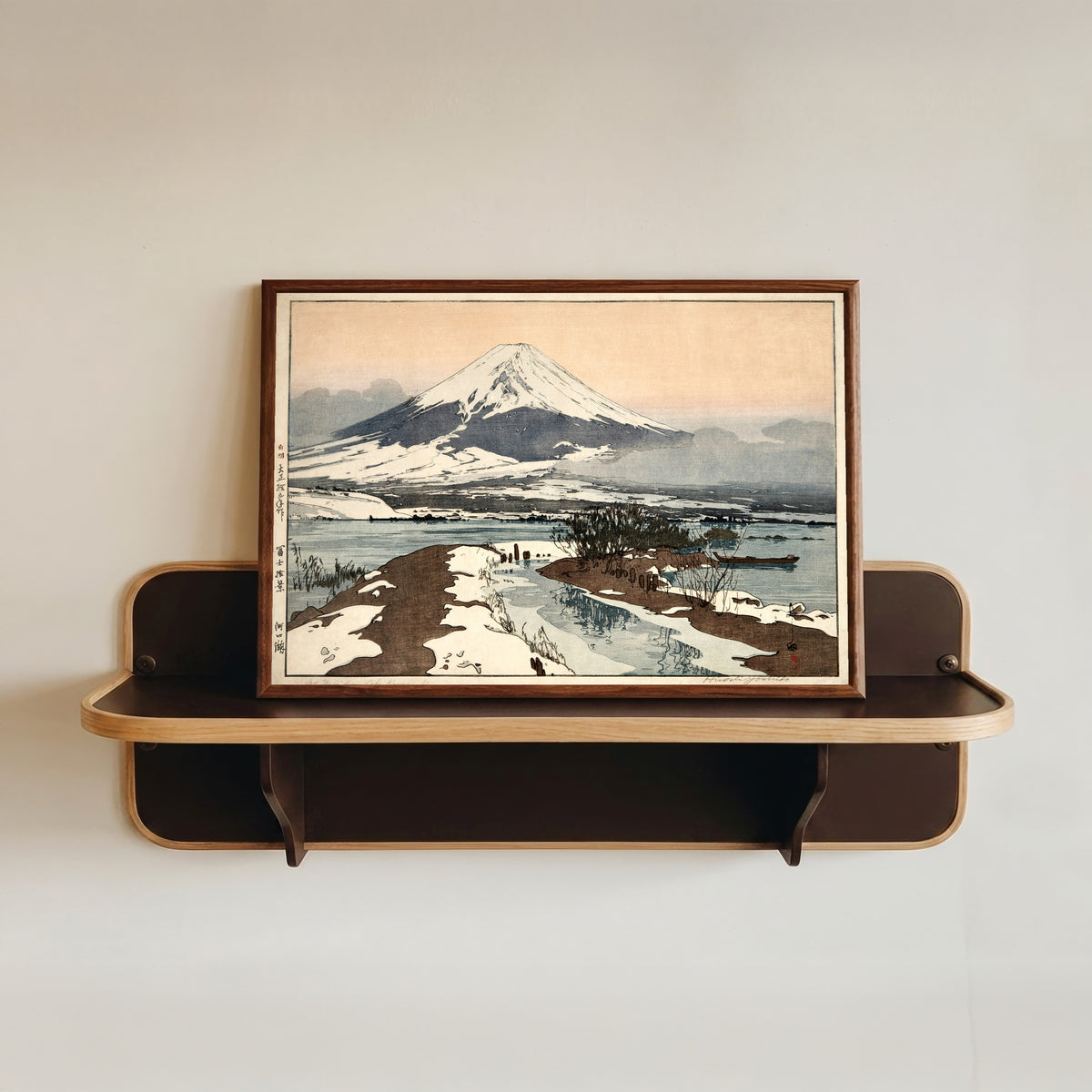 Framed art print of Fuji from Lake Kawaguchi by Hiroshi Yoshida, in a dark wood frame resting on a wall shelf