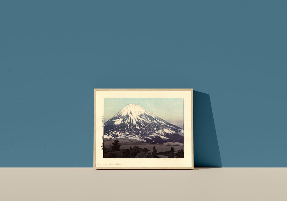 Framed art print of Fujiyama from Gotemba by Hiroshi Yoshida, in a light wood frame leaning on a blue wall
