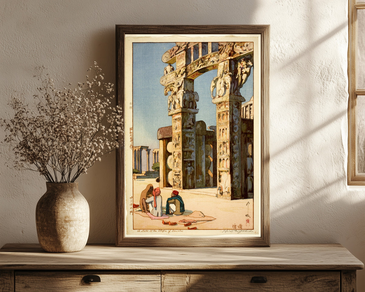 Framed art print of Gate to the Stupa at Sanchi, India by Hiroshi Yoshida, in a dark wood frame leaning on a rustic console beside dried flowers