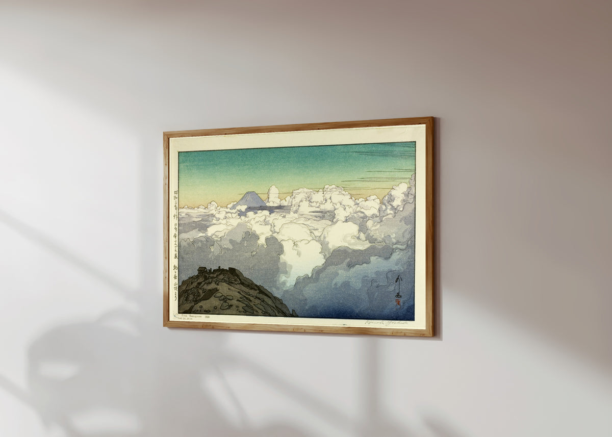 Framed art print of Komagatake Mountain by Hiroshi Yoshida, in a light wood frame on a sunlit white wall, seen at a slight angle