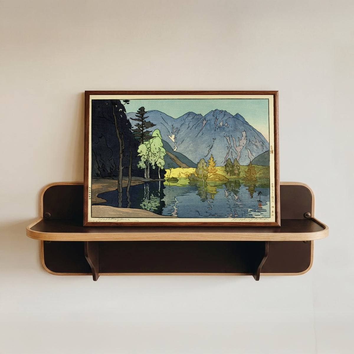 Framed art print of Mount Hodaka by Hiroshi Yoshida, in a dark wood frame resting on a wall shelf